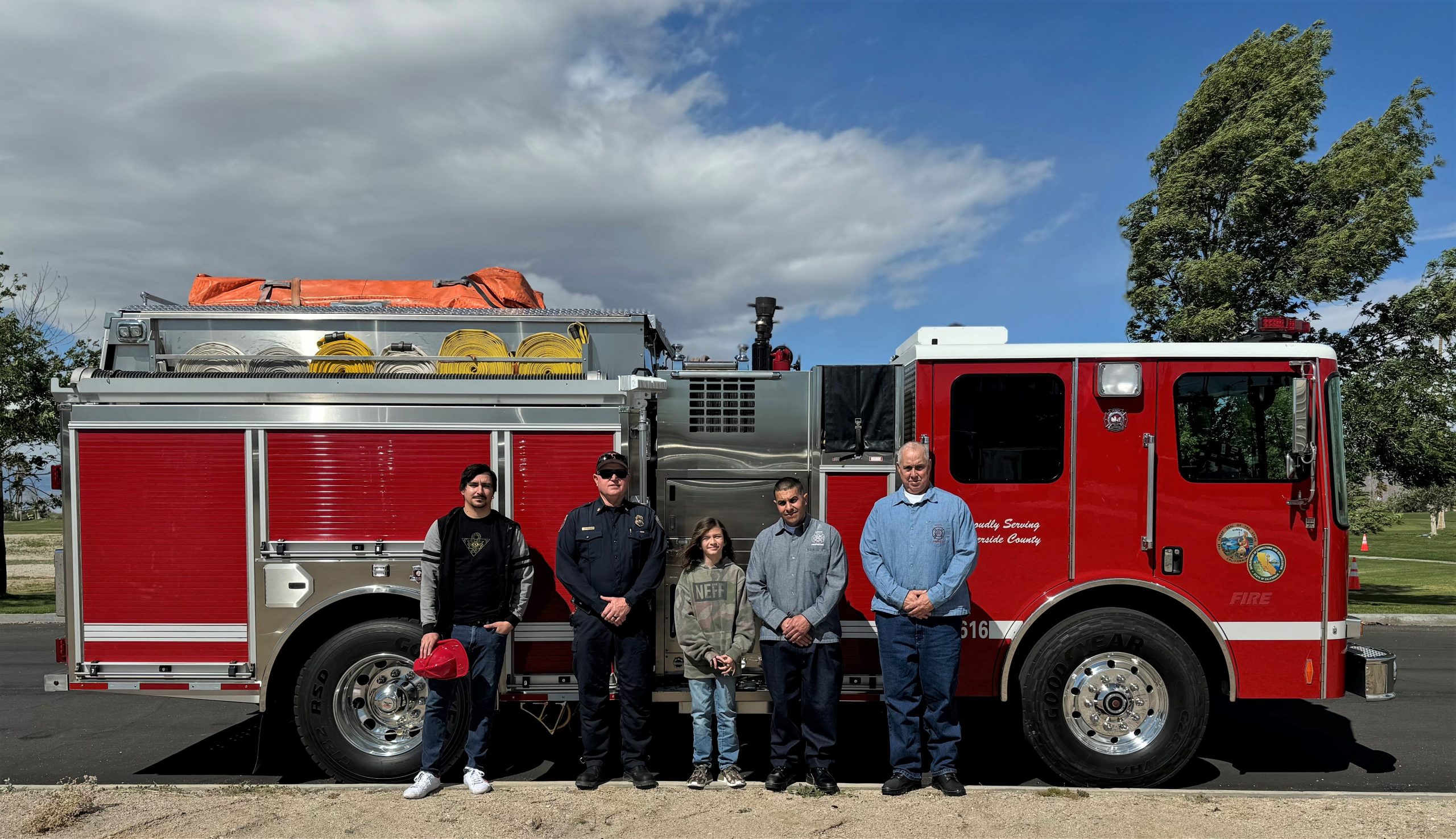 A child and his father with two incarcerated firefighters and a fire chief standing in front of a fire engine.