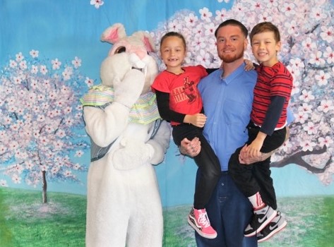 An incarcerated person holds his two young children while posing for a photo with the Easter bunny at Mule Creek State Prison.