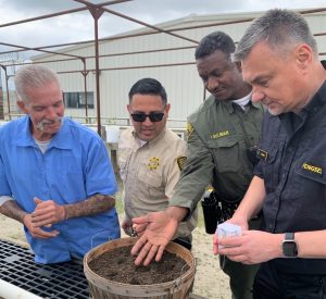 California Model SATF garden reopened with staff and an incarcerated person standing around a planter.