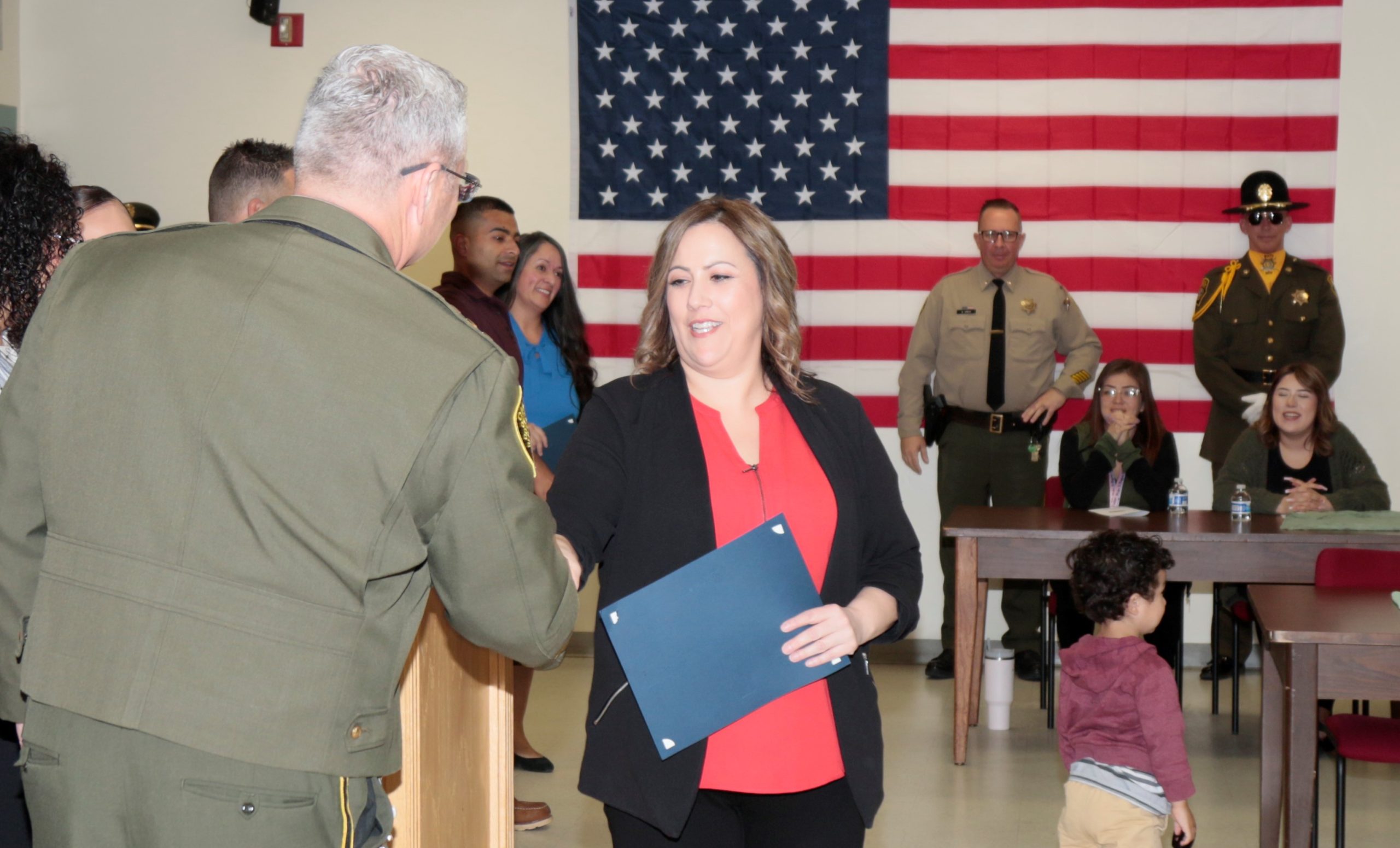 SATF warden shakes hands during a promotion ceremony. The American flag can be seen in the background.
