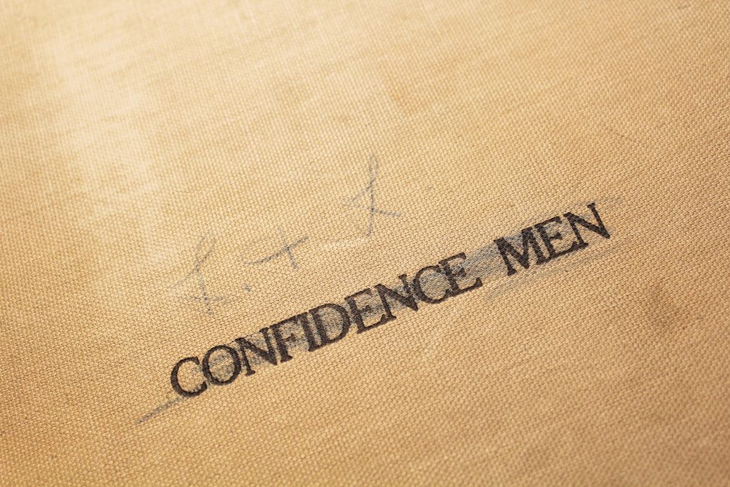 A canvas-bound book cover with the words "confidence men" printed on it.