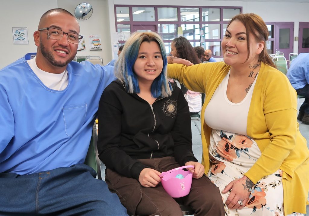 Incarcerated man with a girl and her mother at High Desert State Prison. The girl is holding an Easter basket.