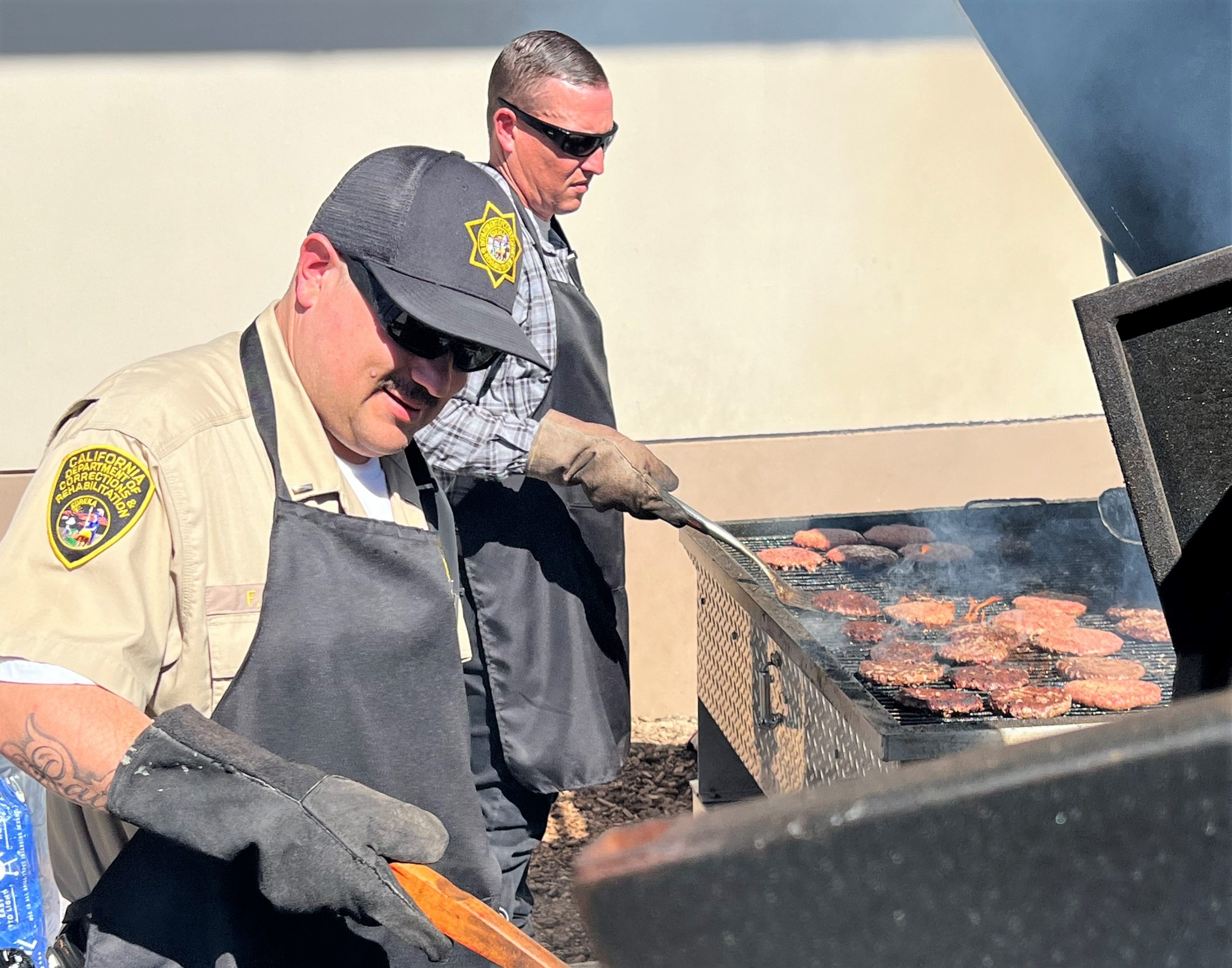 Two people flip burgers on a large barcue.