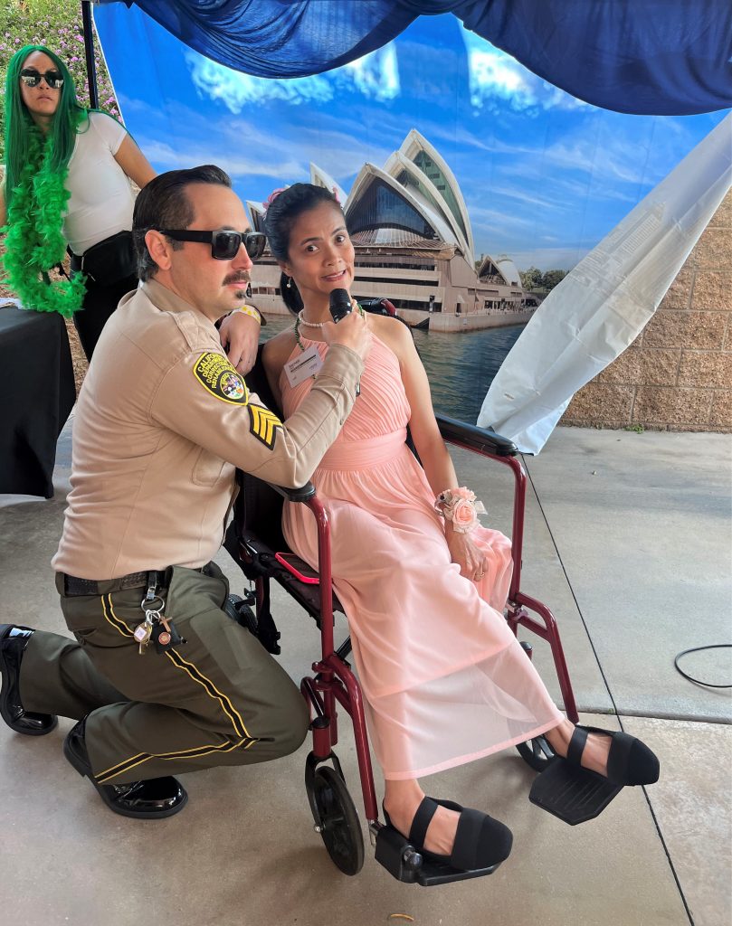 A correctional sergeant with a woman in a wheelchair. He's holding a microphone for her.