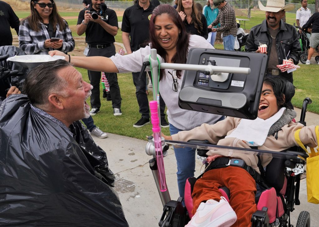A man holds open his mouth as people prepare to throw a pie at his face.