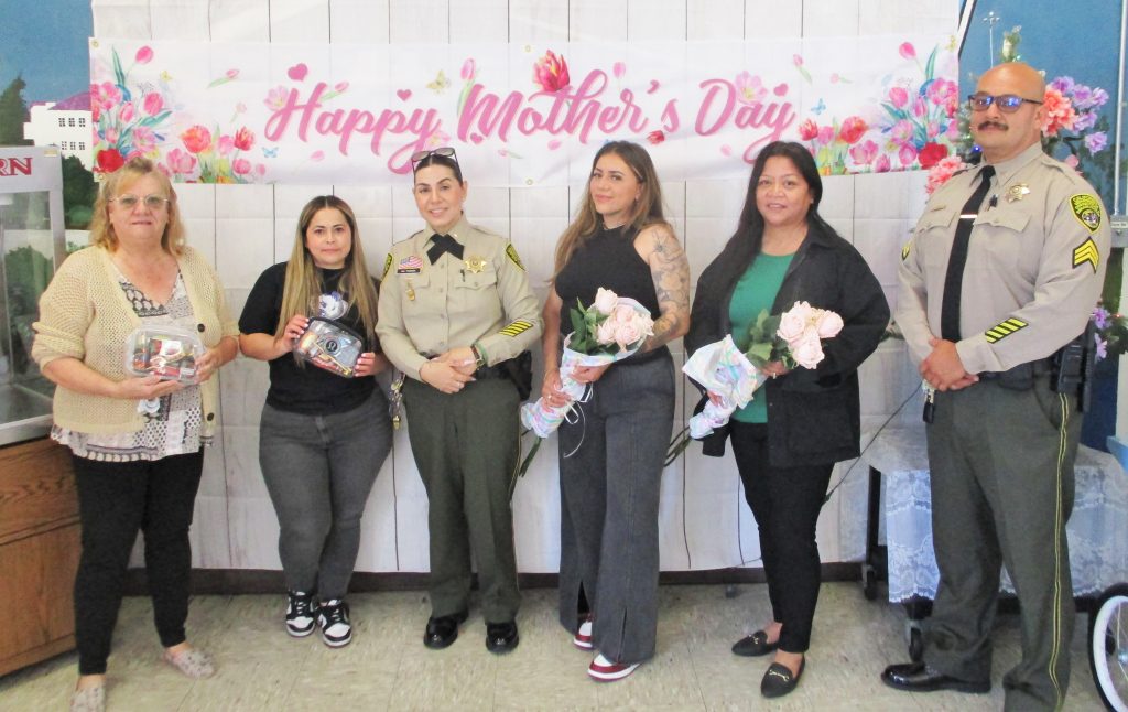 Two prison staff members and four women holding flowers.
