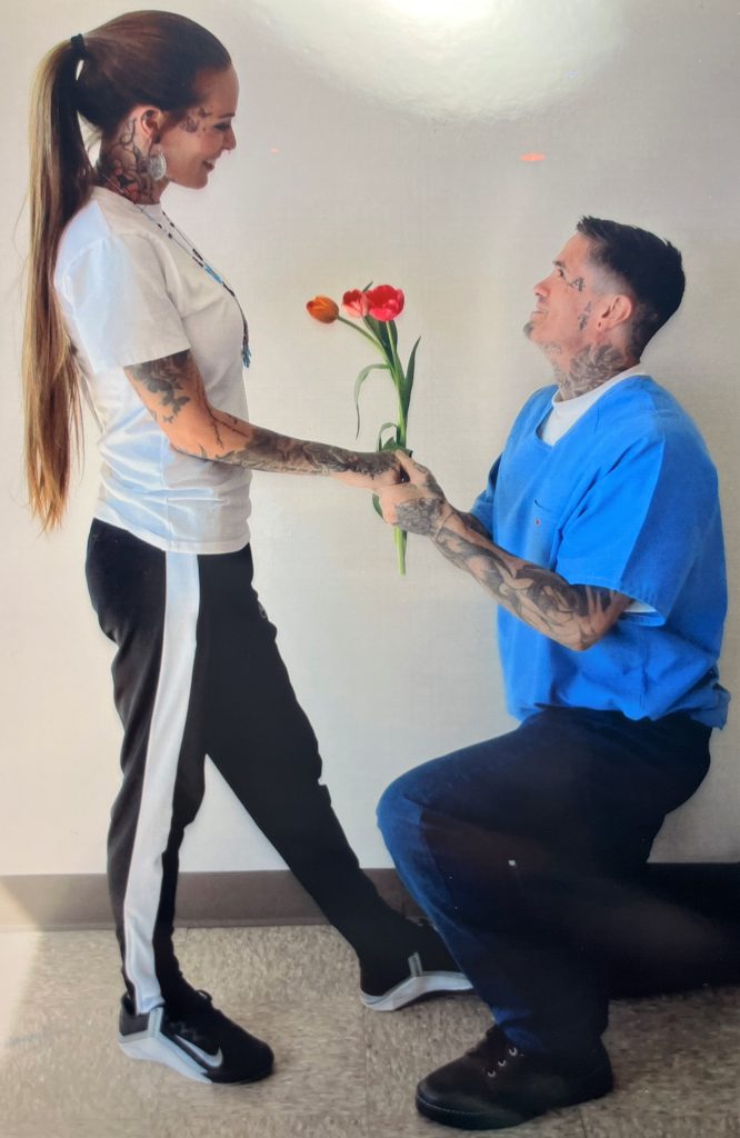 An incarcerated man bends on one knee to present flowers to a visiting woman at High Desert State Prison.