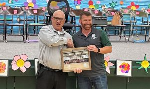 High Desert State Prison warden shakes hands with a school representative while both men hold a photograph.