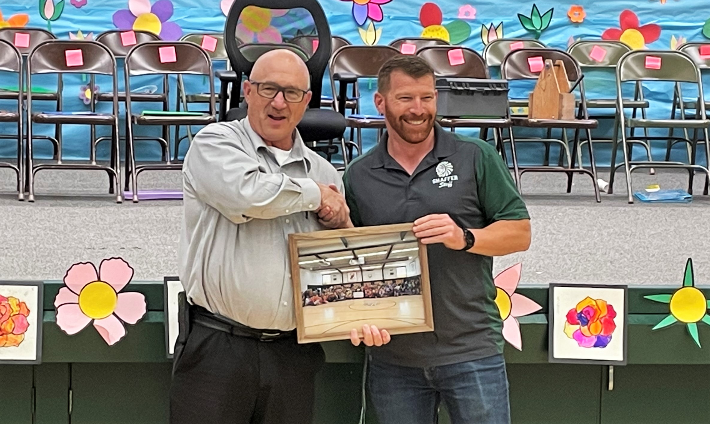 High Desert State Prison warden shakes hands with a school representative while both men hold a photograph.