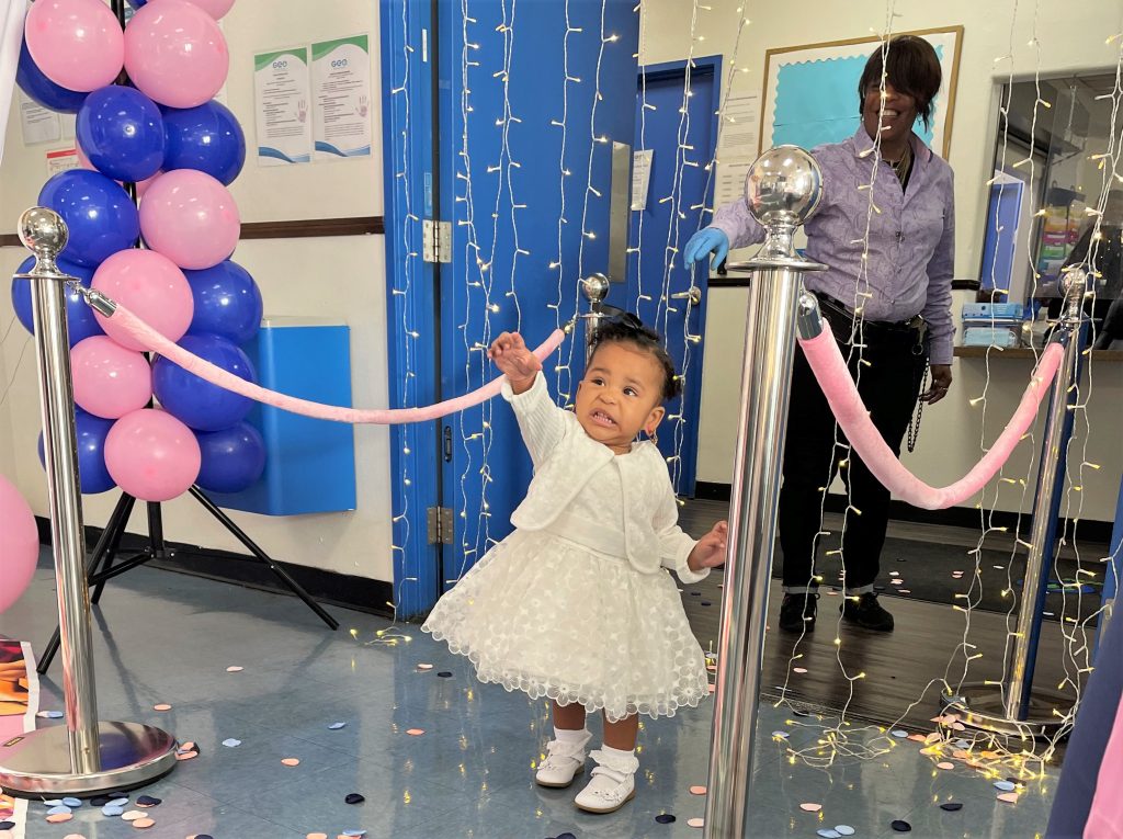 Little girl wearing a white dress and shoes in a decorated dance area.