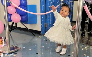 Little girl wearing a white dress and shoes in a decorated dance area.