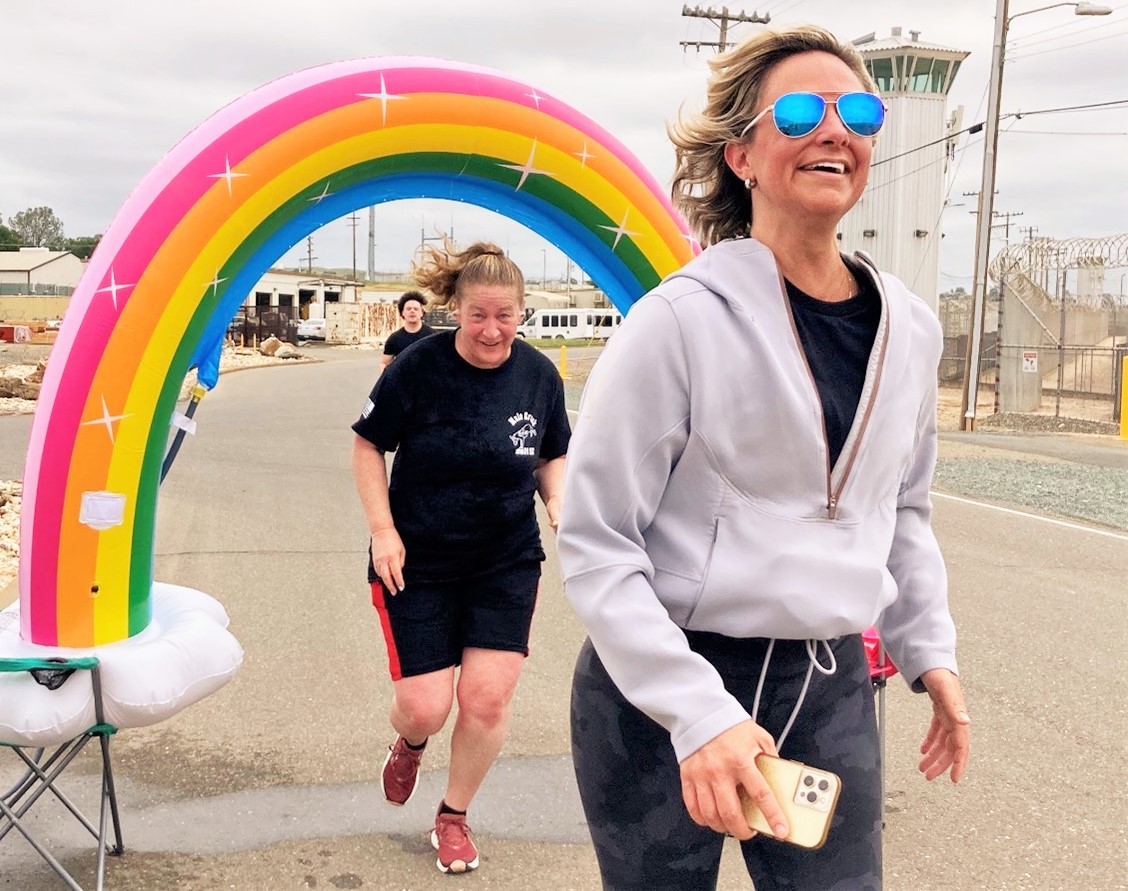 Mule Creek State Prison Fun Run with two women jogging under a water spraying inflatable rainbow.
