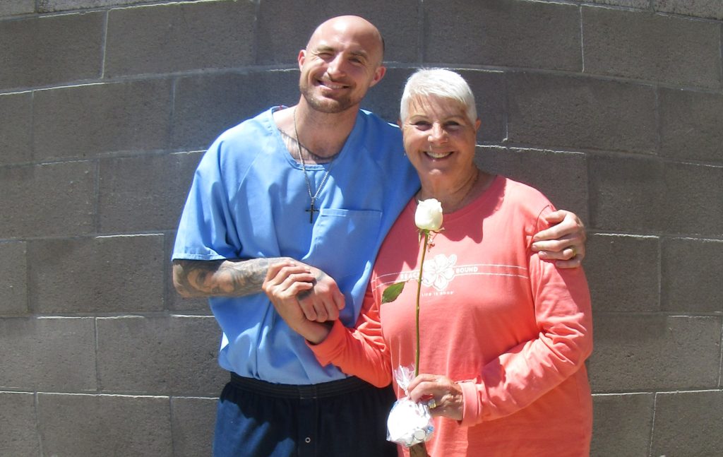 A woman holds a rose while being hugged by her incarcerated loved one.