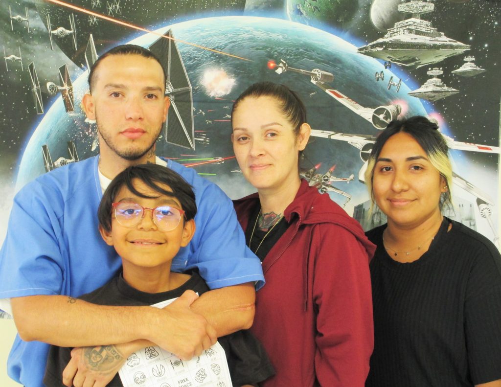 Two people and two kids in front of a Star Wars photo backdrop.