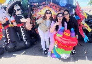 Three women laugh while at a booth representing Mexico at a staff appreciation event at Valley State Prison.