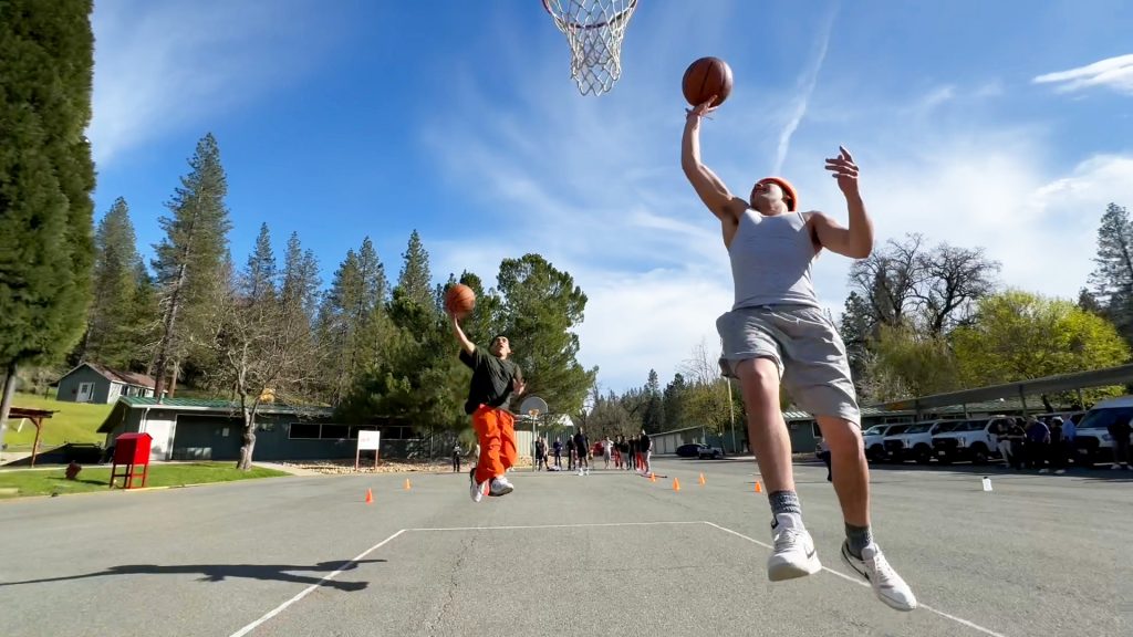 Two people with basketballs go for a basket.