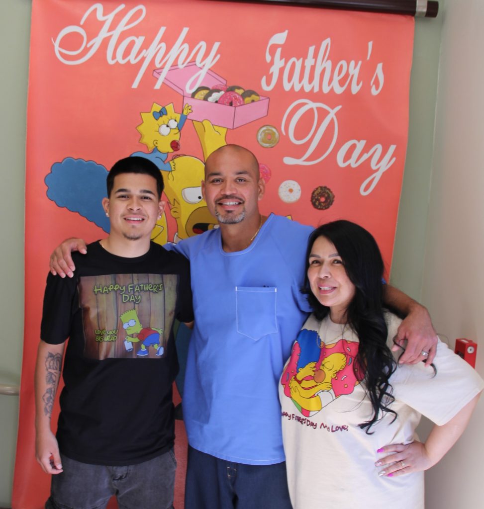 A father, mother and son in front of a Father's Day banner at CHCF visiting during Donuts with Dads.