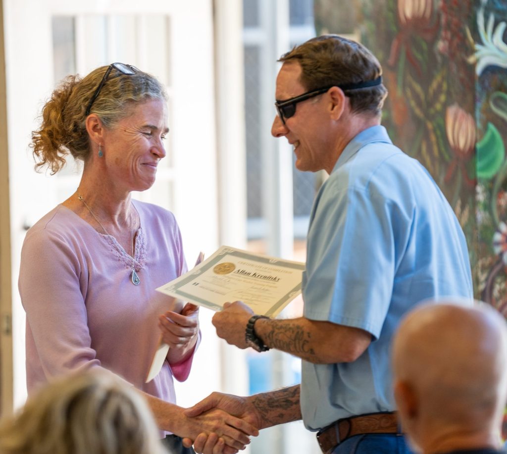 Palliative Care graduation at CMF with a woman handing a certificate to an incarcerated man.