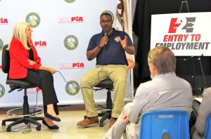 Entry to Employment and CALPIA with a man holding a microphone while speaking to a gathering.