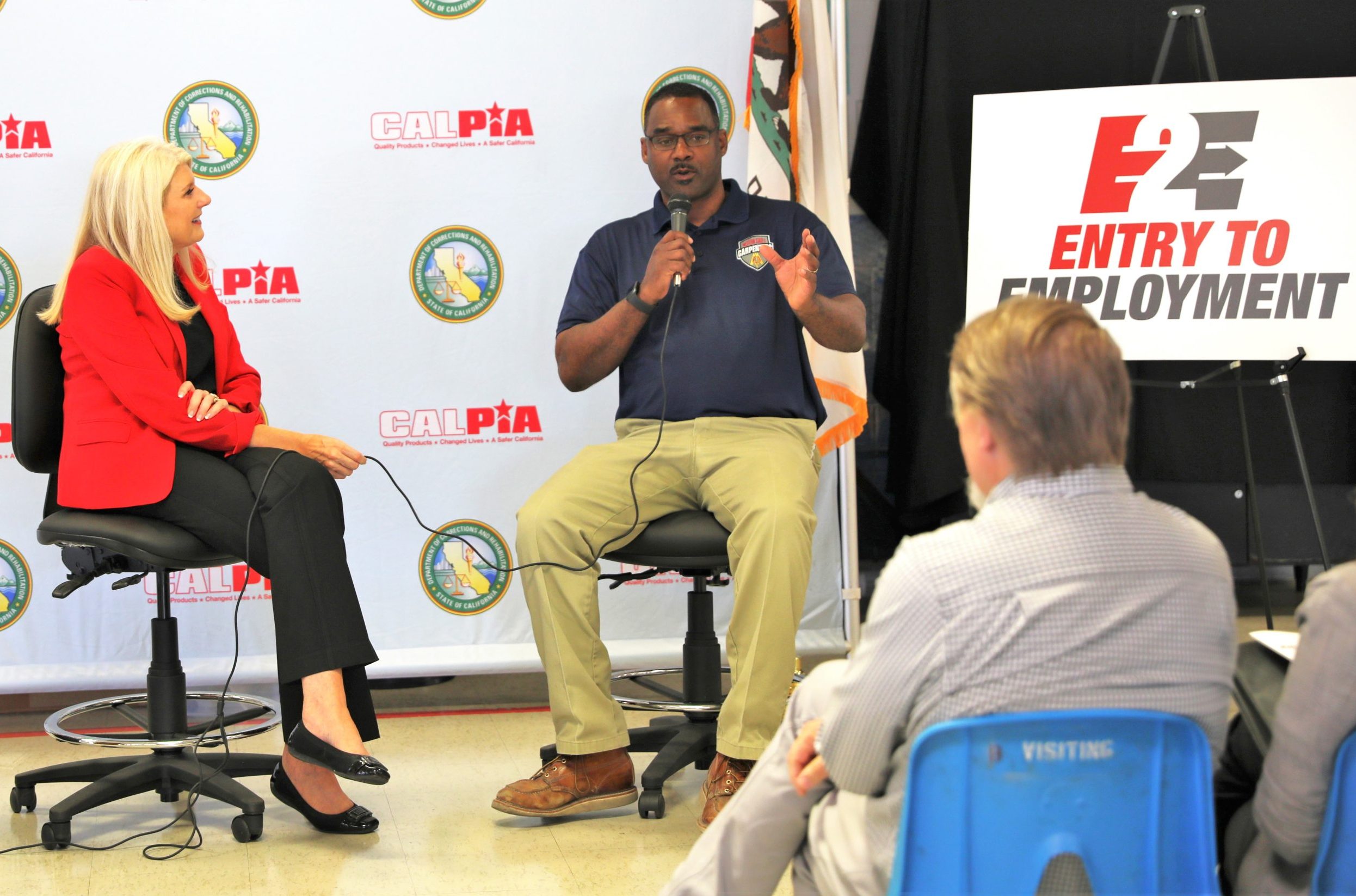 Entry to Employment and CALPIA with a man holding a microphone while speaking to a gathering.