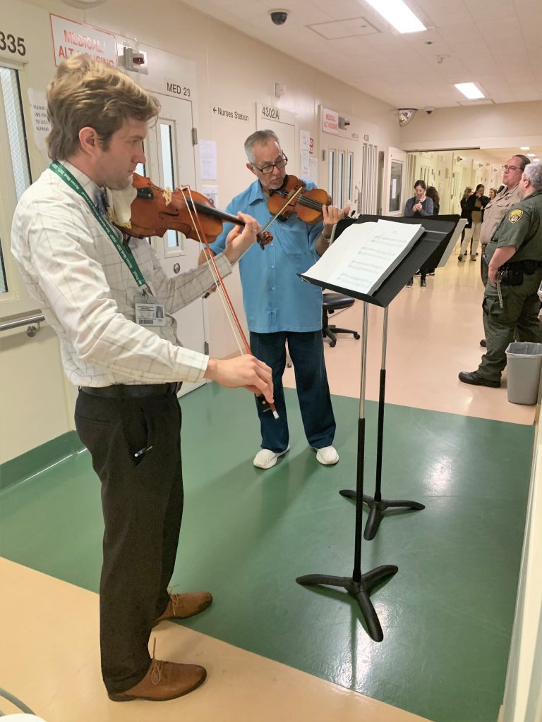 A psychiatrist and incarcerated person perform on violins to demonstrate the healing power of music at San Quentin Rehabilitation Center.