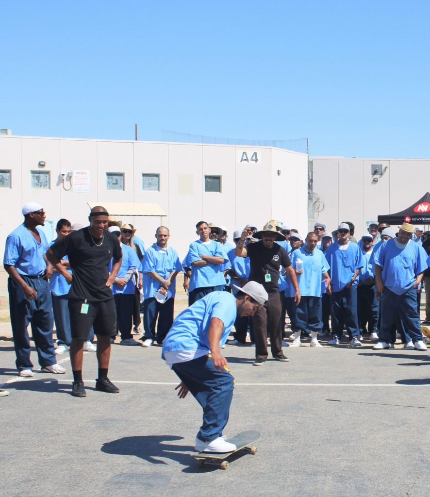 A group watches an incarcerated person riding a skateboard at X-Fest at Centinela State Prison.