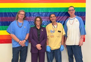 California Health Care Facility Warden Jones with three incarcerated people standing in front of a Pride flag at a banquet event.