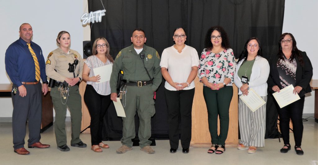 Staff hold certificates while the warden and chief deputy warden look on during the third promotion ceremony at SATF.