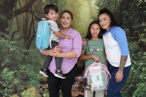 A family with two children holding backpacks to prepare them for going back to school.