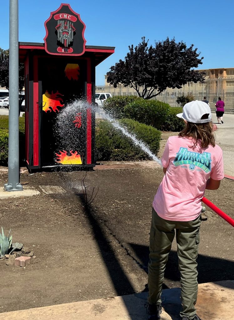 A child sprays fake flames using a firehose. 
