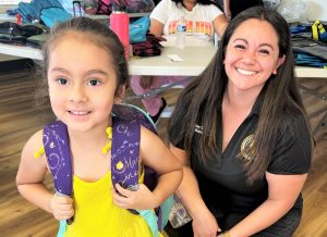 A child smiles while wearing a new backpack stuffed with school supplies.