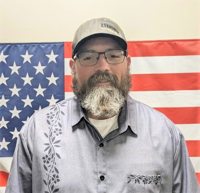 A parole agent, who helped the victims of a car accident, stands in front of an American flag.