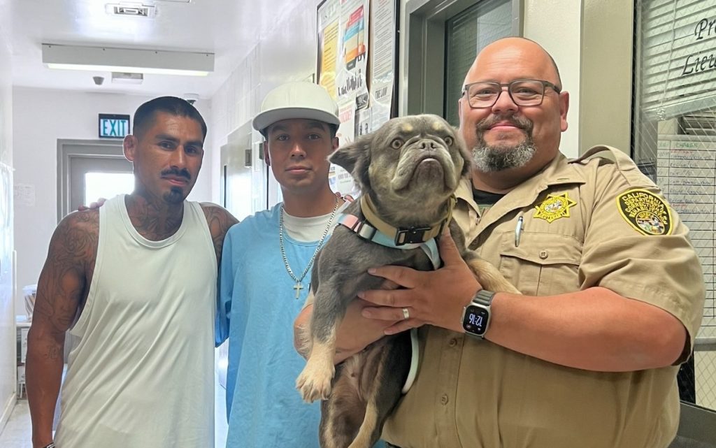 A CDCR lieutenant, his adopted dog, and two incarcerated trainers pose for a photo in the hallway of Pleasant Valley State Prison.