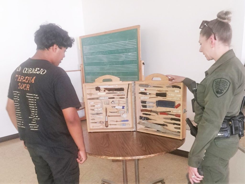 Weapons manufactured by incarcerated people are displayed with a high school student and a correctional officer looking at the display case.