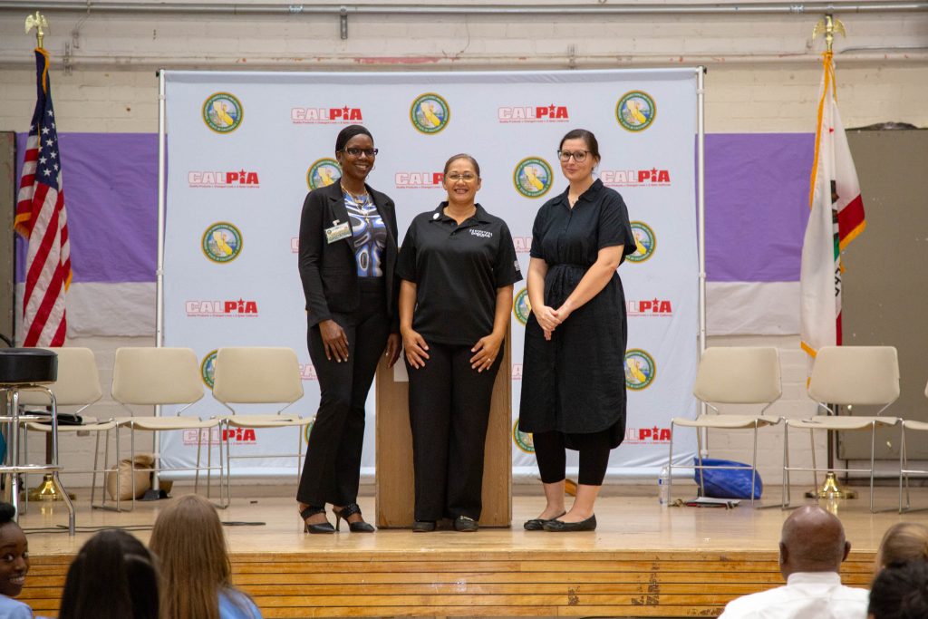 Three women on a stage at CIW for the CALPIA job certifications graduation.