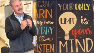 Teacher Pedro Rios at Avenal State Prison with an inspirational board behind him.