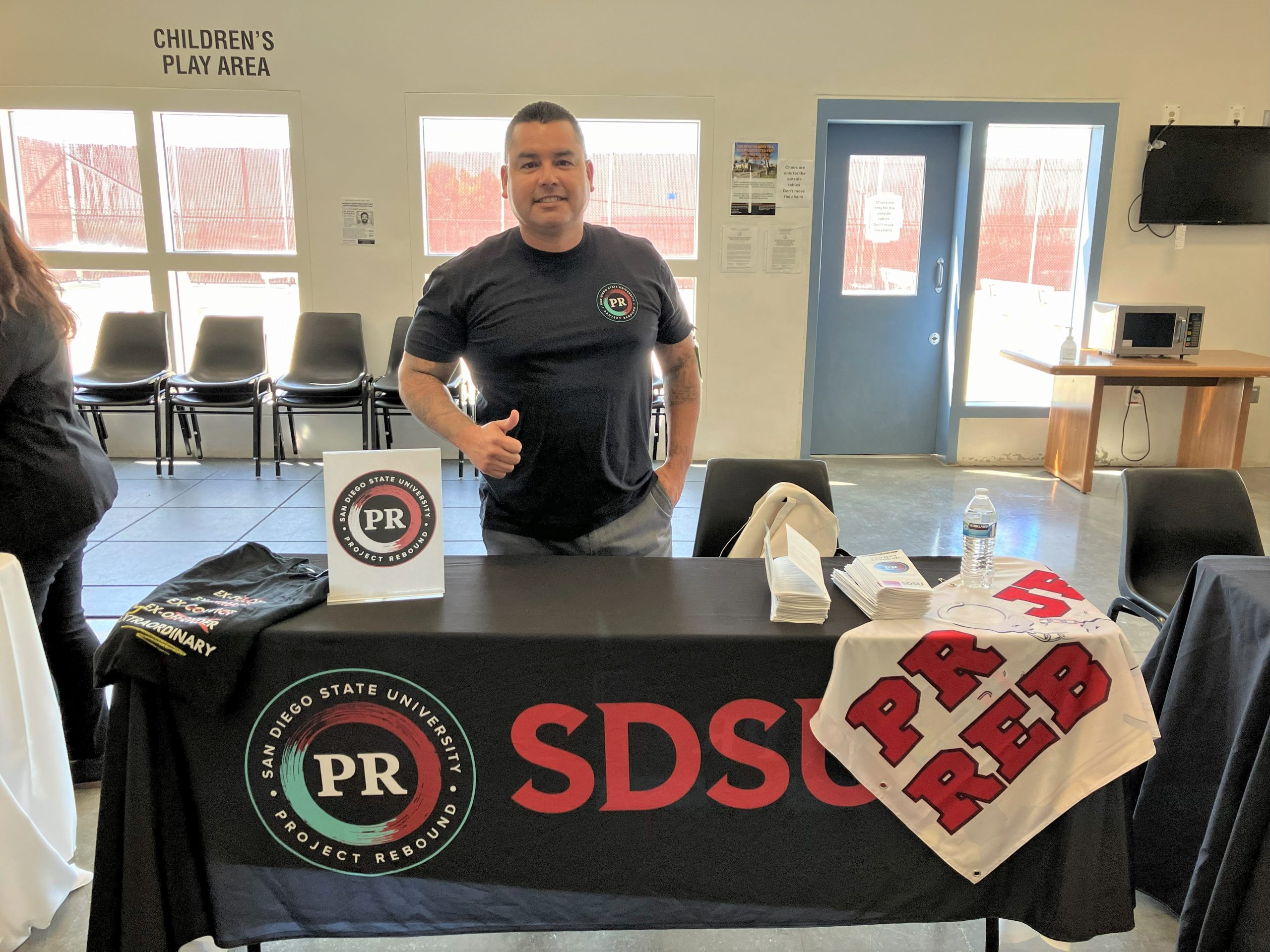 Man stands behind information table for San Diego State University and Project Rebound.