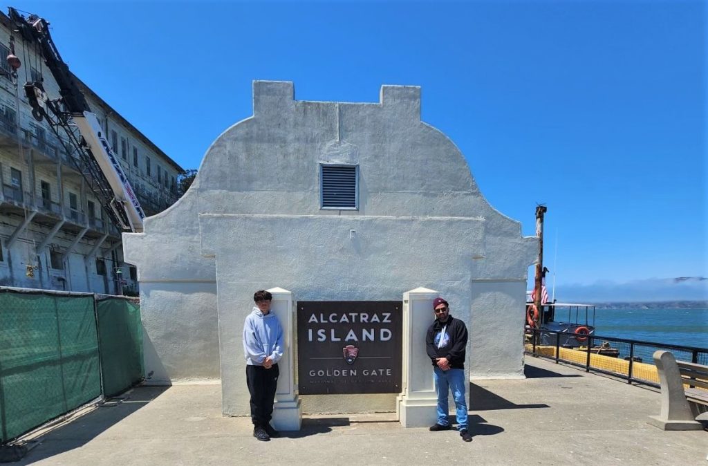 Two people stand beside Alcatraz Island park sign during a San Quentin staff visit.