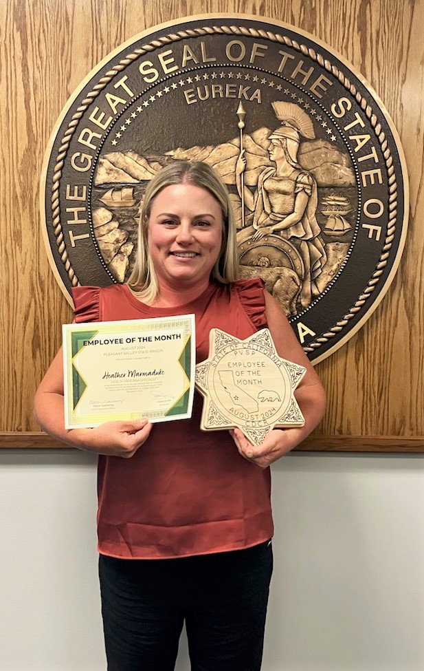 Heather Marmaduke holding employee of the month certificate and a wooden award.