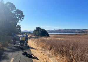 Staff riding along a field with water in the background for Bike the Bridges to benefit Special Olympics Northern California.
