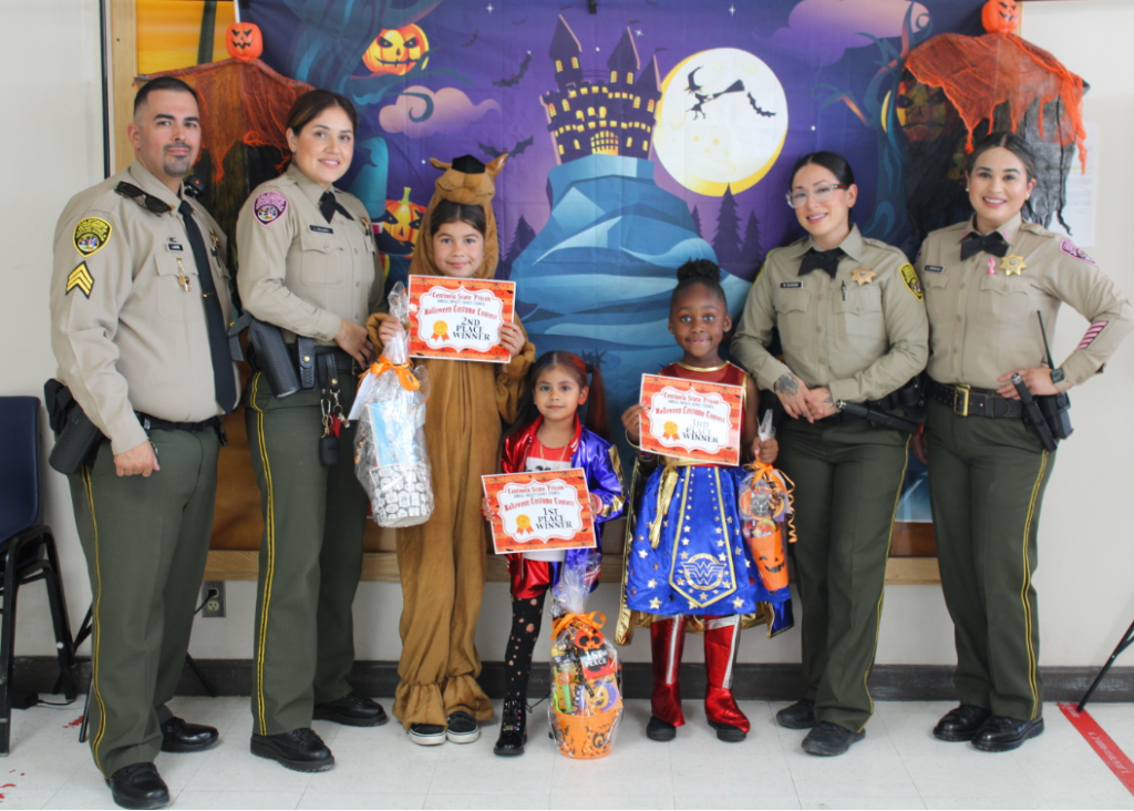 Four visiting staff pose with three children wearing costumes at Centinela State Prison.