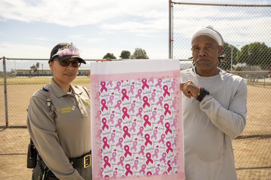 Incarcerated person and a staff member with a banner of names of people who've passed away from cancer.