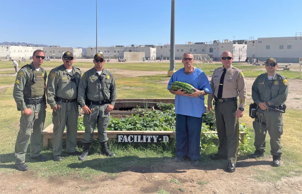 Micro gardens at Ironwood State Prison with an incarcerated person holding a watermelon with multiple staff members standing beside him.