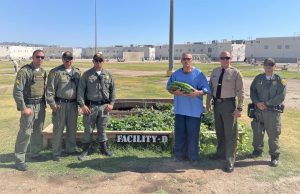 Micro gardens at Ironwood State Prison with an incarcerated person holding a watermelon with multiple staff members standing beside him.