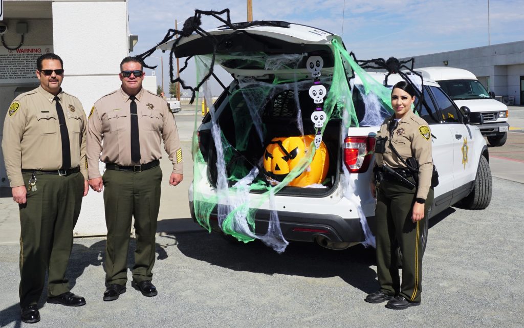 Three correctional officers beside a decorated vehicle trunk.
