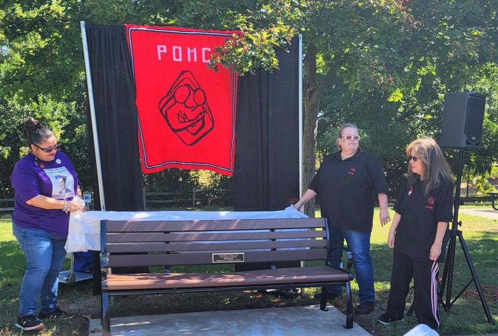 A bench with the POMC flag behind it. POMC stands for Parents of Murdered Children.