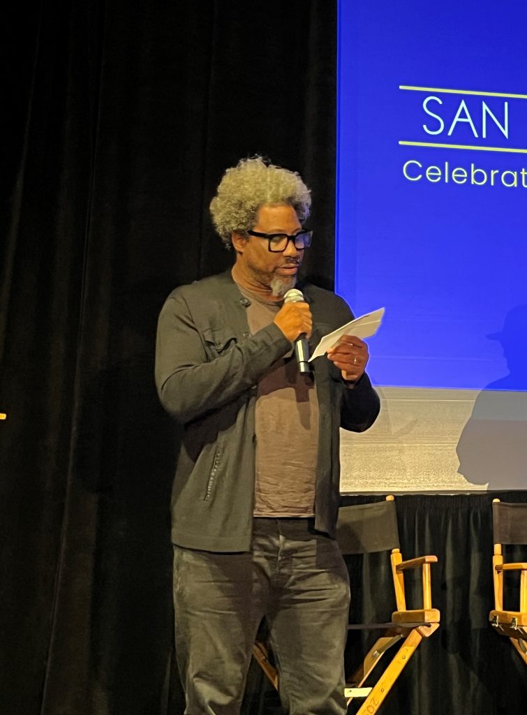 W. Kamau Bell speaks into a microphone at San Quentin.
