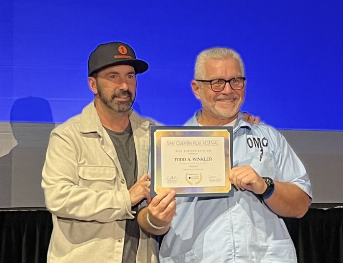 Incarcerated person holds award alongside a film festival volunteer.
