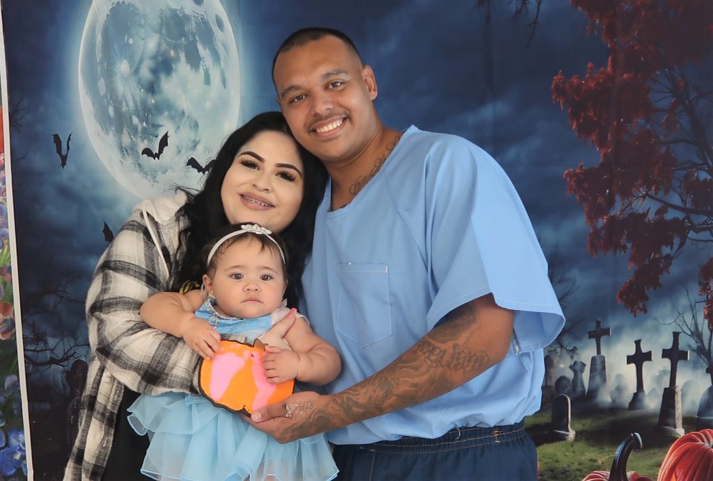 Families enjoyed the visiting event for Halloween. The photo shows a baby holding a decoration and her parents, one of them incarcerated.