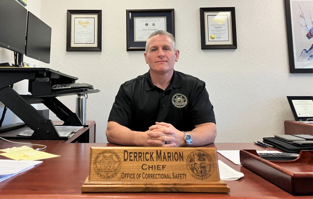 Retiring Chief Derrick Marion, with the Office of Correctional Safety, sits at his desk with his name plaque prominently displayed in the foreground.
